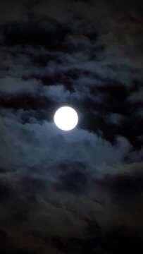 A full moon in the sky with clouds at night. A full moon on a dark cloudy night, an eerie feeling of mysticism. Vertical video for shorts.