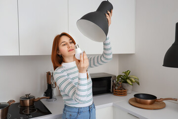 Pretty young woman changing light bulb in kitchen