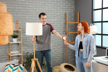 Young woman and man changing light bulbs in lamps at home - obrazy, fototapety, plakaty