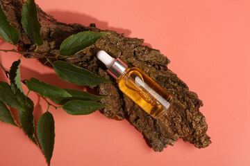 Bottle of cosmetic oil with tree bark and leaves on red background