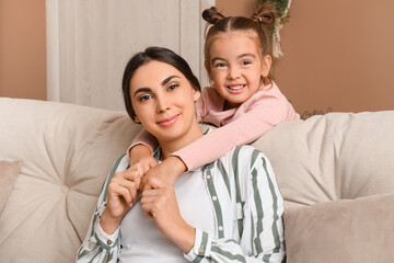 Happy mother with her little daughter sitting on sofa in living room and hugging