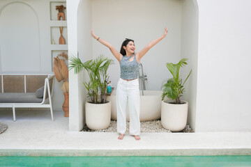 Full body of Asian young woman in pattern top and white pants spreading arms feeling excited while...