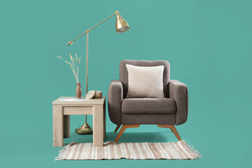 Cozy armchair with cushion, coffee table and standard lamp on turquoise background