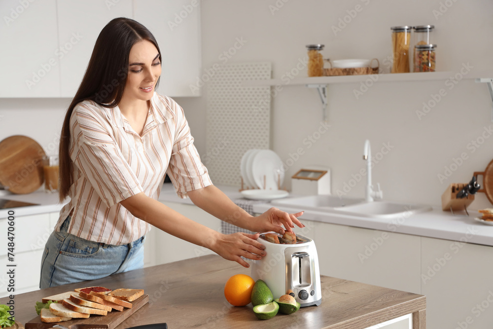 Wall mural Young beautiful happy woman making tasty toasts in kitchen