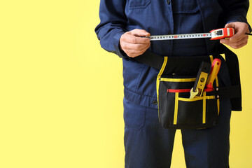 Male construction worker with measuring tape and tools on yellow background, closeup