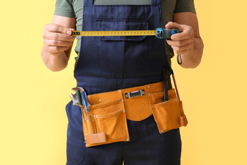 Male construction worker with measuring tape and tools on yellow background, closeup