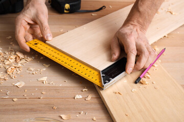 Male carpenter measuring wooden plank with square ruler in workshop, closeup