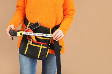 Female construction worker with measuring tape and tools on beige background, closeup