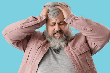 Fototapeta premium Portrait of sad senior man desperately holding head on blue background