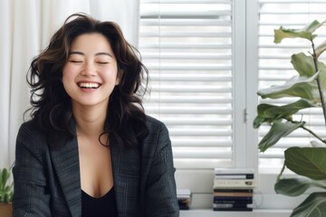 Asian woman sits in a chair in front of a window, smiling happily