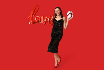 Beautiful young happy woman with gift box and balloon in shape of word LOVE on red background....