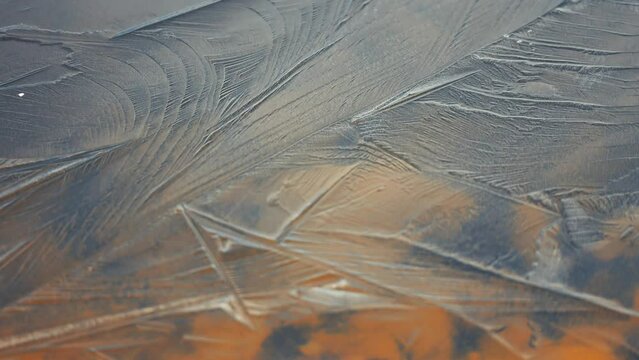 On the surface of a shallow lake with a rocky bottom, abstract patterns form on the thin, transparent ice.
