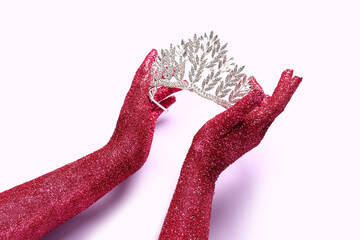 Female hands covered with glitter and beautiful tiara on lilac background, closeup