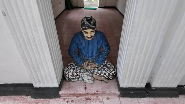 Statue of Abdi Dalem or Sultan of Yogyakarta servants sitting cross-legged wearing blangkon, batik and traditional clothing near palace entrance gate.
