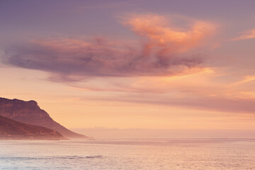 Ocean, sunset and calm water by mountain and tourism destination for summer vacation in nature. Blue sky, clouds and neon color on cape town beach, peace and outdoor travel with sunshine in paradise