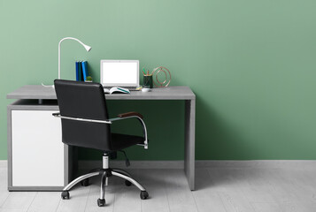 Modern office workplace with laptop and armchair near green wall