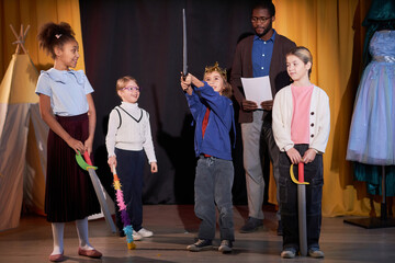 Full length portrait of young boy playing valiant prince on stage in school play with group of children - Powered by Adobe