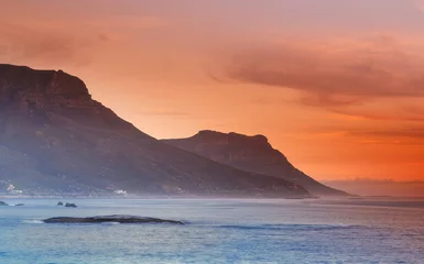 Photo sur Plexiglas Plage de Camps Bay, Le Cap, Afrique du Sud Ocean, sunset and mountains in nature or sustainable environment and travel destination for vacation. Landscape, sea or sunlight on water on beach, calm or seascape of camps bay for tourist adventure