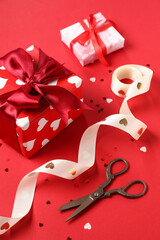 Beautiful gift boxes with ribbon, scissors and confetti on red background. Valentines Day...