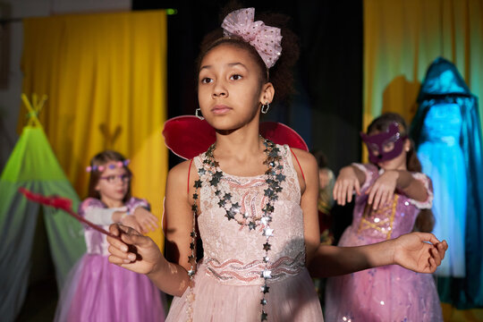 Portrait of Black teen girl playing fairy on stage in theater and holding magic wand in spotlight