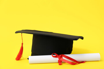 Mortar board and diploma on yellow background
