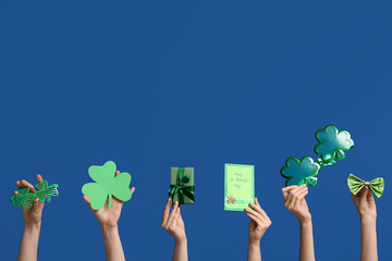 Female hands holding gift box and party decor for St. Patrick's Day celebration on blue background...