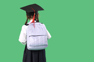 Little girl in graduation hat with backpack on green background, back view. End of school year