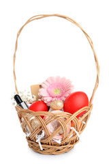 Wicker basket with decorative cosmetics, Easter eggs and flowers isolated on white background