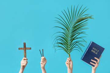 Female hands with wooden cross, nails, palm leaf and Holy Bible on color background. Good Friday...