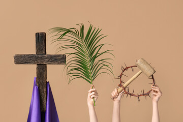 Female hands with wooden cross, palm leaf, wooden mallet and and crown of thorns on color...