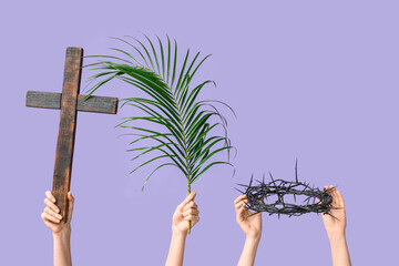 Female hands with wooden cross, palm leaf and crown of thorns on lilac background. Good Friday...