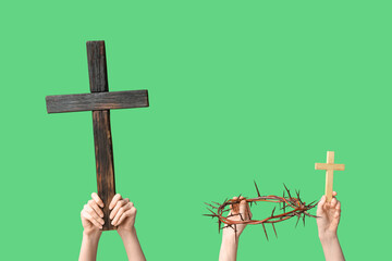 Female hands with wooden crosses and crown of thorns on green background. Good Friday concept