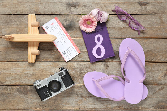 Composition with beach accessories, toy plane, passport and ticket on wooden background. International Women's Day