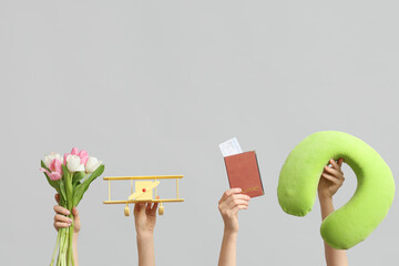 Female hands with travel pillow, passport, toy plane and flowers for International Women's Day on grey background