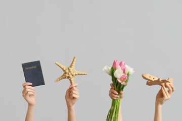 Female hands with wooden toy plane, passport, starfish and flowers for International Women's Day on grey background