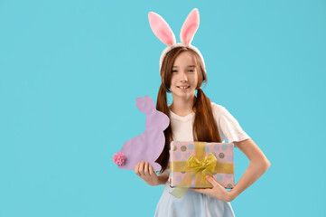Cute little girl with Easter bunny ears, paper rabbit and gift on blue background