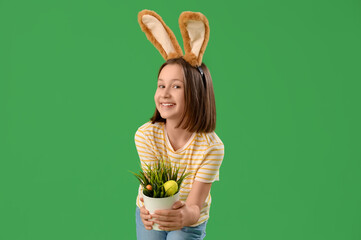 Cute little girl with Easter bunny ears and plant with hidden eggs on green background
