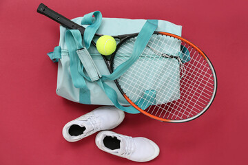 Sports bag with sportswear, tennis rackets and ball on red background