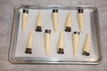 A baking tray with dough rolled on cone molds ready for baking.
