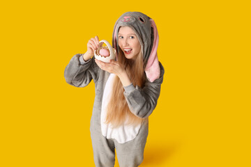 Beautiful young happy woman in bunny costume holding basket with egg on yellow background. Easter...