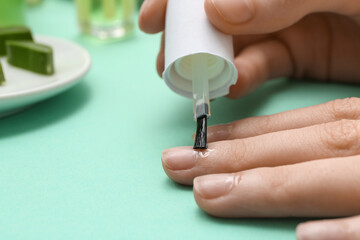 Woman applying cuticle oil onto fingernails on turquoise background, closeup