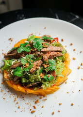 A close-up of a salad with sliced chicken breast, avocado, and nuts on a white plate