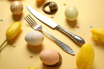 Cutlery for table setting with Easter eggs and yellow tulips on color background