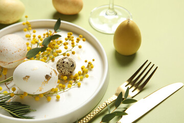 Beautiful table setting with Easter eggs and mimosa flowers on green background