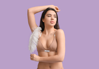 Beautiful young woman with soft feather on lilac background. Epilation concept