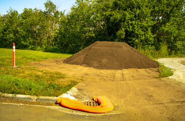 A pile of topsoil on the edge of park open space field with filter sock on front ground to protect drainage system