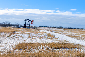 A oil pump jack in an agriculture field at winter season with multiple power lines on background