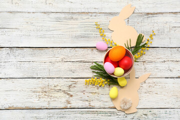 Basket with painted Easter eggs decorated with mimosa flowers on white wooden background