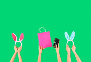 Women with payment terminal, shopping bag and bunny ears on green background. Easter Sale
