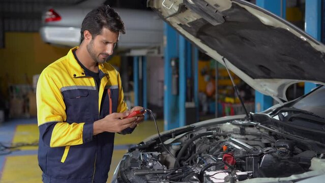 happy latin auto mechanic man checking electric battery voltage maintenance with digital battery tester in garage cars service . hispanic technician repairing vehicle at garage . auto repair shop